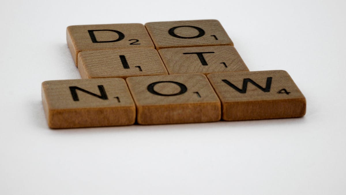 Wooden Scrabble tiles spelling 'Do It Now' on a white background. Motivational concept.